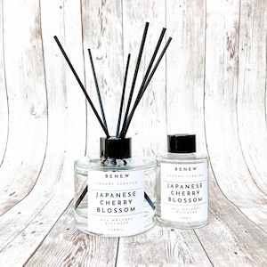 May include: Two clear glass bottles with black lids and black diffuser sticks. The bottles are labeled "BENEW LUXURY SCENTED JAPANESE CHERRY BLOSSOM ALL NATURAL DIFFUSER 150ML" and "BENEW LUXURY SCENTED JAPANESE CHERRY BLOSSOM ALL NATURAL DIFFUSER 10ML".
