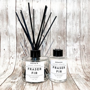 May include: Two clear glass bottles with black lids and black diffuser sticks. The bottles are labeled "BENEW LUXURY SCENTED FRASER FIR ALL NATURAL DIFFUSER 150 ML" and "BENEW LUXURY SCENTED FRASER FIR ALL NATURAL DIFFUSER 70 ML".
