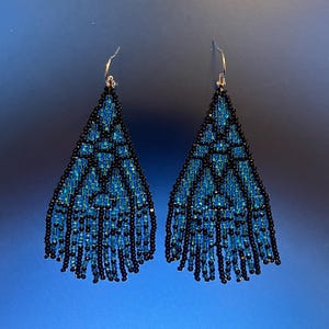 May include: A pair of beaded earrings in a triangular design. The earrings are made with black and blue beads, with a fringed edge. They have silver-coloured ear wires.