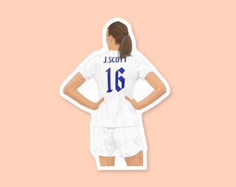 May include: A sticker featuring a woman in a white soccer uniform with the name "J. SCOTT" and the number "16" in blue. The woman is viewed from the back, with her hands on her hips. The sticker has a white border and a peach background.