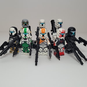 May include: A collection of eight plastic toy soldier minifigures featuring various colored armor patterns including green, orange, red, and black. Each figure wears a helmet with a blue visor and carries a black plastic toy blaster weapon.