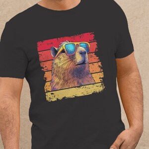 May include: A dark gray t-shirt with a retro-style graphic of a marmot wearing sunglasses. The graphic is set against a colorful striped background.