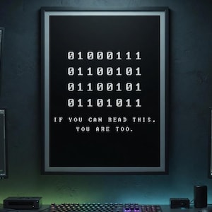 Pode incluir: Um poster preto emoldurado com código binário branco e o texto "IF YOU CAN READ THIS, YOU ARE TOO." A imagem mostra uma configuração de computador com monitores exibindo código, um teclado e um mouse, com tema de programação.