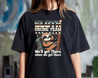 May include: A black short-sleeved t-shirt featuring a graphic of a brown sloth wearing a green backpack and clinging to a tree. The text reads SLOTH HIKING TEAM and We'll get There when we get there, accompanied by a row of five white stars.