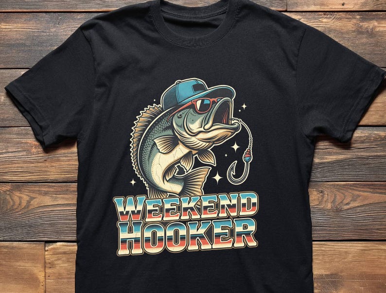 May include: Black t-shirt featuring a cartoon bass wearing a blue cap and sunglasses, with a fishing hook in its mouth. The text "WEEKEND HOOKER" is displayed in a retro font, with blue, red, and cream colors.