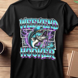 May include: Black t-shirt featuring a cartoon fish wearing sunglasses and a cap, with the words "WEEKEND HOOKER" in a blue and purple gradient font. The design includes lightning bolt graphics.