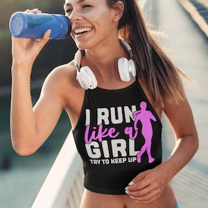 Puede incluir: Un top corto negro con un gráfico blanco que dice "I run like a girl try to keep up" con una silueta rosa de una mujer corriendo.