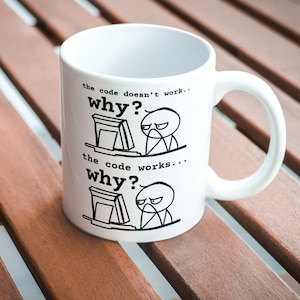 May include: White ceramic mug with a black and white illustration of a person at a computer. The text on the mug reads "the code doesn't work... why?" and "the code works... why?"