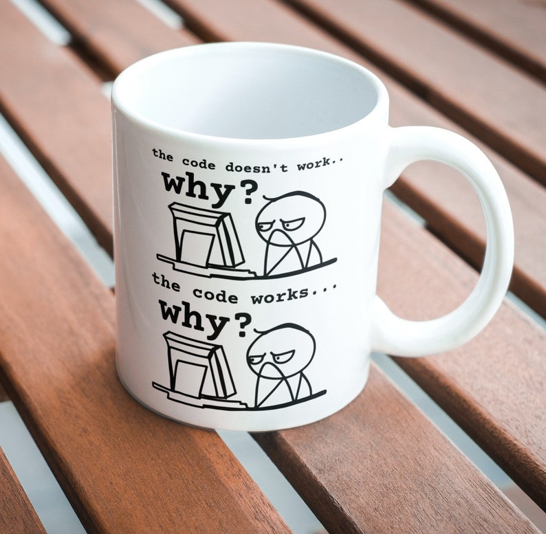 May include: White ceramic mug with a black and white illustration of a person at a computer. The text on the mug reads "the code doesn't work... why?" and "the code works... why?"