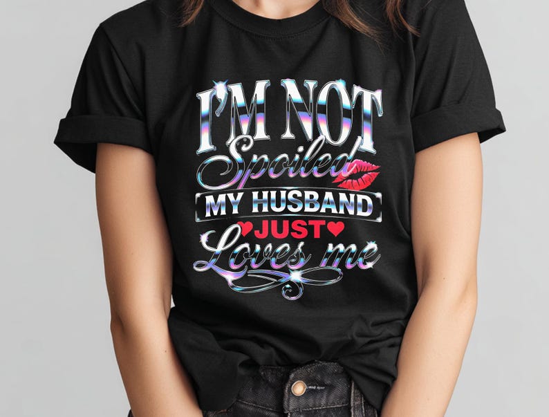 Puede incluir: Camiseta negra con el texto "I'M NOT Spoiled MY HUSBAND JUST Loves me" en una fuente hologr&aacute;fica. El dise&ntilde;o incluye un beso de labios rojos y un coraz&oacute;n rojo. Una prenda casual.