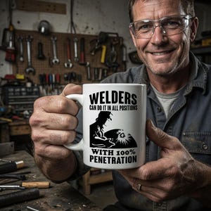 Pu&ograve; includere: Tazza in ceramica bianca con la scritta "WELDERS CAN DO IT IN ALL POSITIONS WITH 100% PENETRATION" in nero. La tazza presenta la silhouette di un saldatore al lavoro. La tazza &egrave; tenuta da una persona.