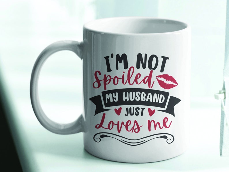Puede incluir: Taza de cer&aacute;mica blanca con asa curva. La taza presenta el texto "I'M NOT Spoiled MY HUSBAND Just Loves me" en letras negras y rojas, con una huella de labios roja y acentos de coraz&oacute;n. La taza est&aacute; dise&ntilde;ada para parejas.