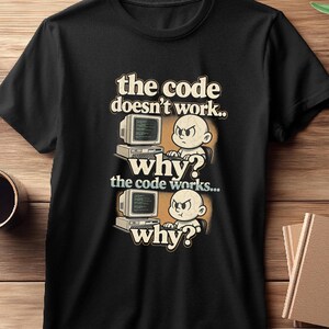 May include: Black t-shirt with a retro-style graphic. The design features a cartoon baby with an angry expression in front of a computer, with the text "the code doesn't work.. why? the code works... why?"
