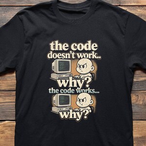 May include: Black t-shirt with a humorous graphic. The design features a cartoon baby with an angry expression in front of a computer, with the text "the code doesn't work.. why? the code works... why?"