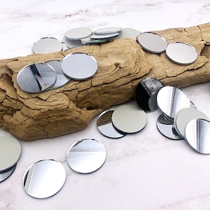 May include: A pile of round, silver-colored, decorative mirror tiles on a piece of driftwood.
