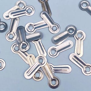 May include: A collection of small, silver-colored metal turn buttons, each featuring a flat, elongated body with a rounded end containing a single circular hole for mounting. These hardware fasteners are scattered across the frame.
