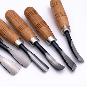 May include: Set of six wood carving tools with wooden handles and metal blades. The tools have different shapes and sizes.