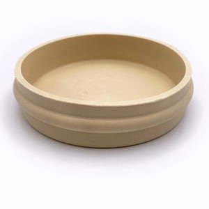 May include: A beige round silicone lid with a raised edge. The lid is designed to fit on top of a container.
