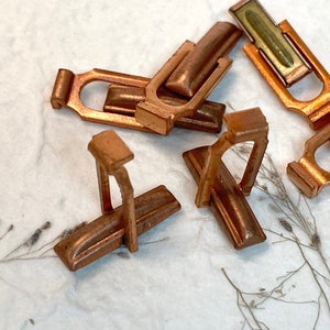 May include: Five copper-colored metal connectors with a green insert. The connectors have a unique shape and are designed for electrical connections.