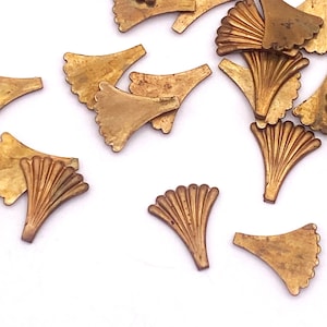 Könnte beinhalten: Eine Sammlung von goldfarbenen Ginkgo-Blatt-Anhängern aus Metall. Die Anhänger sind auf einer weißen Oberfläche verstreut und haben ein detailliertes, fächerartiges Design.