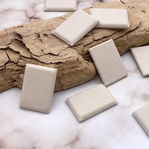 May include: A collection of 12 off-white rectangular ceramic tiles with a rough texture. The tiles are scattered on a piece of driftwood and a marble surface.