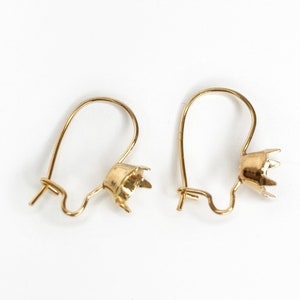 Puede incluir: Un par de cierres de pendientes dorados con un engaste en forma de corona. Los cierres son de metal y tienen un diseño simple y elegante.