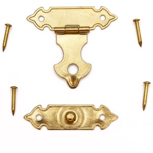 May include: A set of brass-colored decorative hardware, including a hinged clasp, a base plate with a central knob, and four small nails. The hardware has an ornate, vintage design, perfect for small boxes or chests.