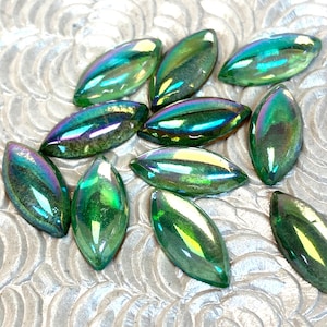 May include: A group of iridescent green glass teardrop-shaped beads. The beads have a pearlescent finish and are scattered on a white background.