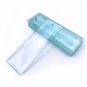 May include: A stack of clear glass tiles with beveled edges. The tiles are arranged in a staggered pattern, with the top tile slightly offset from the others. The tiles are all the same size and shape, and they have a smooth, polished surface.