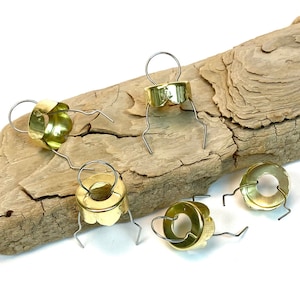 May include: Five gold bottle stoppers with a wire loop and a decorative edge. The stoppers are on a piece of driftwood.
