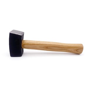 May include: A mallet featuring a solid, dark-colored rectangular head and a smooth, light-brown wooden handle. The tool is positioned horizontally, showcasing the contrast between the dark, dense head and the natural grain of the wooden handle.