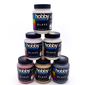 May include: A pyramid of six jars of Hobby Colorobbia glaze. The jars are white with black lids and labels. The labels have the word "GLAZE" and the color name. The colors include white, pink, pearl, flesh, and gray. Each jar contains 4 fl oz.