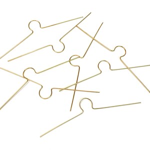 以下が含まれることがあります： 中央に円形のループと垂直方向の延長部を備えた直線状の水平バーを特徴とする、金色の金属ワイヤー部品のコレクション。白い背景に対して散らばったパターンで配置されています。