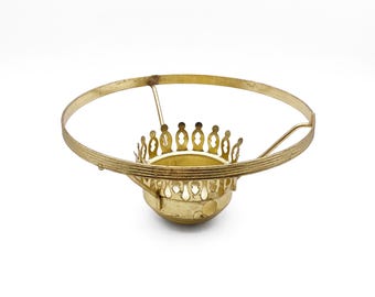 May include: A gold-toned metal lamp shade fitter featuring a circular outer ring with a ribbed texture and a central, crown-like gallery with decorative cutouts. The component includes three support arms connecting the outer ring to the center.