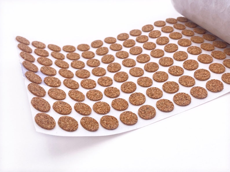 Puede incluir: Una hoja de c&iacute;rculos de corcho marr&oacute;n sobre un fondo blanco. Los c&iacute;rculos est&aacute;n dispuestos en filas y tienen un di&aacute;metro de aproximadamente 2,5 cm.