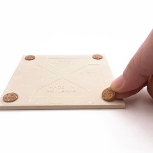 Puede incluir: Un posavasos de cer&aacute;mica beige con almohadillas de corcho en la parte inferior. El posavasos tiene el texto "Lanka Wall Tile" y "Made in Sri Lanka" impreso en &eacute;l.