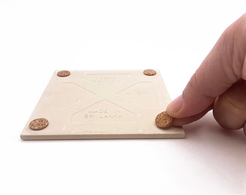 Puede incluir: Un posavasos de cer&aacute;mica beige con almohadillas de corcho en la parte inferior. El posavasos tiene el texto "Lanka Wall Tile" y "Made in Sri Lanka" impreso en &eacute;l.