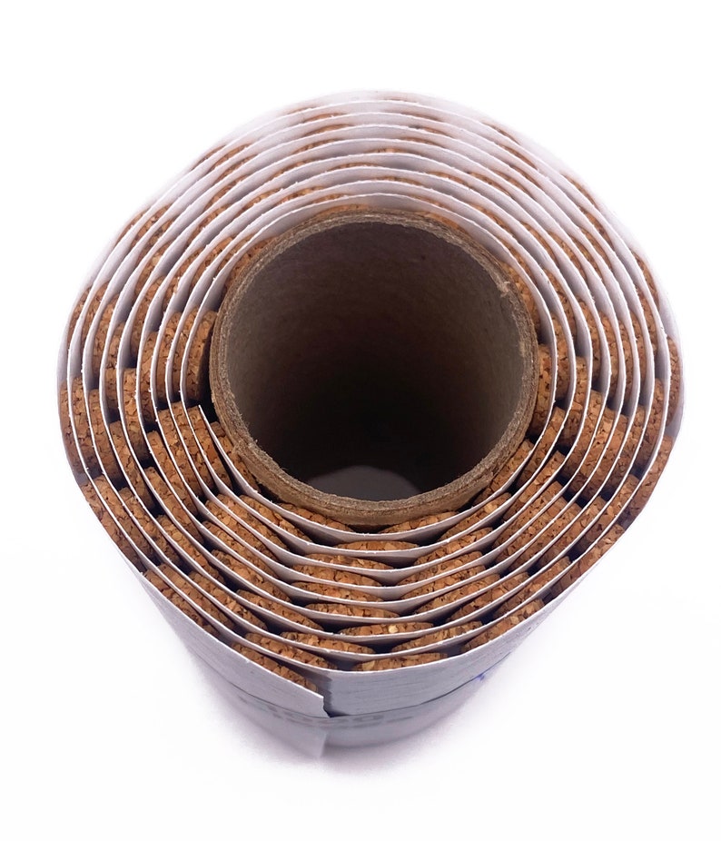 Puede incluir: Un rollo de baldosas de corcho, enrollado y asegurado con una etiqueta de papel blanco. Las baldosas de corcho son marrones y tienen una textura natural ligeramente rugosa. El rollo est&aacute; sobre un fondo blanco.