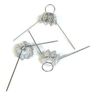 May include: Three silver metal ornament caps with a decorative design and a wire loop. The caps are designed to be placed on the top of Christmas ornaments.