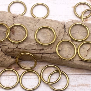 May include: A collection of gold-toned metal jump rings, arranged on a piece of driftwood. The rings are various sizes and are ideal for jewelry making or crafting.
