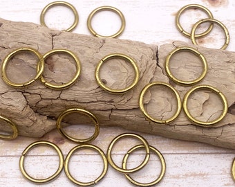 May include: A collection of gold-toned metal jump rings, arranged on a piece of driftwood. The rings are various sizes and are ideal for jewelry making or crafting.