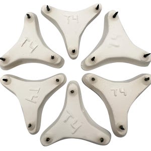 May include: Six white, triangular objects with three black spikes each. Each object has the letters "T4" imprinted on it. The objects are arranged in a circular pattern against a white background.