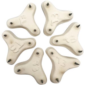 Peut inclure: Six dessous-de-plat en céramique blanche avec trois pointes métalliques sur le dessous. Chaque dessous-de-plat porte l'inscription "T3".