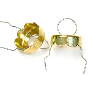 May include: Two gold-colored metal ornament caps with wire loops. The caps have a scalloped edge and are designed to be used for hanging ornaments.