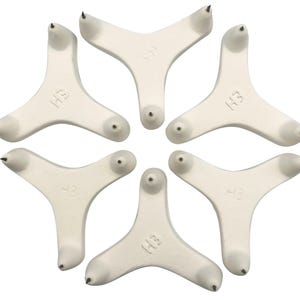 Könnte beinhalten: Sechs weiße Plastik-Dreizack-Tackernadeln mit einer spitzen Spitze an jedem Zacken. Jede Nadel hat die Buchstaben "H3" auf der Oberseite.