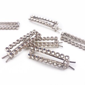 May include: Six silver hair clips with rows of round rhinestones. The clips are all the same size and shape, and they are arranged in a random pattern on a white background.