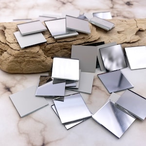 May include: A pile of small, square, silver-backed mirrors. The mirrors are scattered on a light gray marble surface.