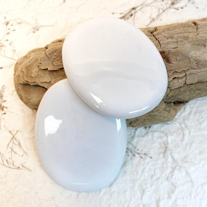 May include: Two smooth, white oval-shaped stones. The stones are glossy and have a slight sheen.
