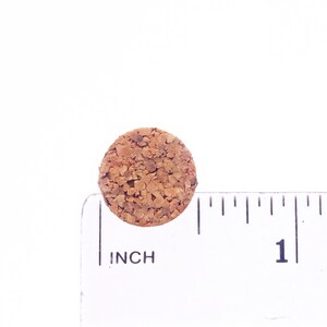 Puede incluir: Un tap&oacute;n de corcho redondo que mide aproximadamente 2,5 cm de di&aacute;metro. El corcho es marr&oacute;n y tiene una textura rugosa.