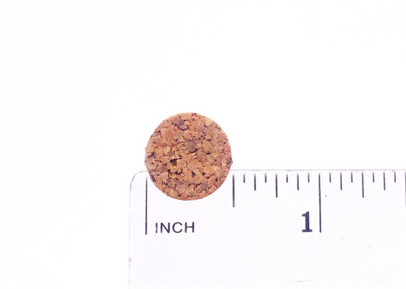 Puede incluir: Un tap&oacute;n de corcho redondo que mide aproximadamente 2,5 cm de di&aacute;metro. El corcho es marr&oacute;n y tiene una textura rugosa.
